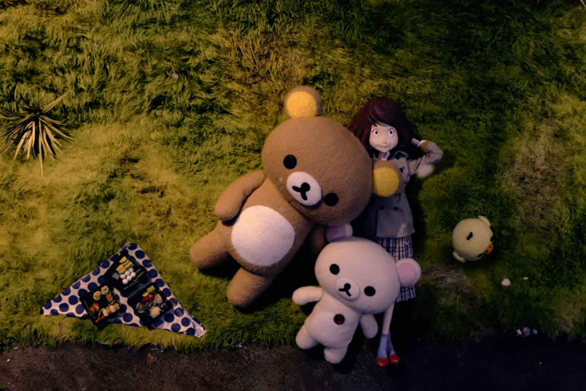 Personagens da série rilakkuma e kaoru deitados na grama com um toalha de piquenique estendida ao lado deles.